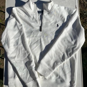 Vit half-zip tröja från Polo Ralph Lauren - Snygg vit långarmad tröja från Polo Ralph Lauren med klassisk half-zip och broderad logga på bröstet. Tröjan har hög krage.  Perfekt för en clean och stilren look.