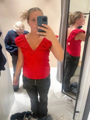 Röd volangtopp med v-ringning - Snygg röd topp med volangdetaljer vid axlarna och djup v-ringning. Toppen är ärmlös och har en figurnära passform som framhäver siluetten. Perfekt för dig som vill sticka ut med färg och detaljer.