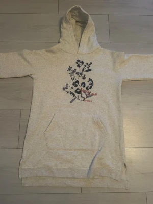Pepe jeans grå hoodie med blommönster - Snygg beige hoodie från Pepe Jeans med blå blommönster på bröstet och röd text. Modellen har huva, lång ärm och en stor magficka. Materialet är mjukt och bekvämt.🤍💕