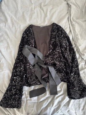 Svart paljettkofta med knytband - Säljer denna superfina glittriga tröja som är helt öppen i ryggen och perfekt till när man vill klä upp sig! Hör gärna av dig vid frågor 🩷