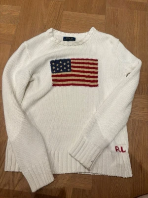 Vit stickad tröja Polo Ralph Lauren - Vit stickad tröja från Polo Ralph Lauren med amerikansk flagga i blått, rött och vitt på bröstet. Tröjan är använd en gång och har alltså nytt skick. ❤️