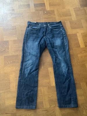 Mörkblå raka jeans från polo ralph lauren - Säljer ett par mörkblå jeans från Replay med raka ben och klassisk femficksmodell. Jeansen har kontrastsömmar och Replay-logga broderad i rött på myntfickan. Tillverkade i slitstark denim, äperfekta för en avslappnad stil.