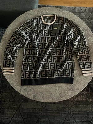 Stickad Fendi Sweatshirt - Snygg stickad tröja från Fendi med ikoniskt FF-mönster i svart och beige. Tröjan har rund halsringning och ribbade muddar i svart och beige. Tillverkad i Italien och har en exklusiv känsla med tydlig logga över hela plagget.