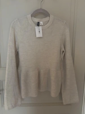 Beige peplumstickad tröja från H&M - Säljer en beige stickad tröja från hm med peplumdetalj i midjan. Tröjan har rund halsringning och långa ärmar. Perfekt för dig som gillar en enkel men ändå trendig look. Materialet känns mjukt och bekvämt. Har även lappen kvar på sig, aldrig använd!