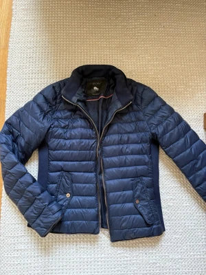 Mörkblå dunjacka från Zara Woman - Snygg mörkblå dunjacka från Zara Woman med quiltad design och dragkedja framtill. Jackan har två fickor med knappstängning och ribbade paneler på sidorna för extra komfort. Perfekt för kalla vinterdagar och stilrena outfits. Passar en i S❤️