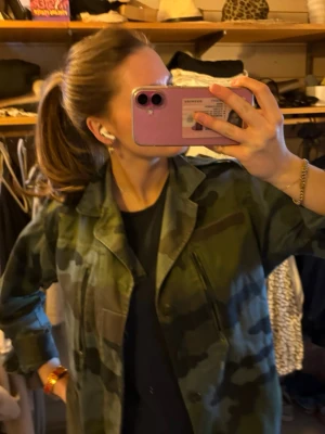 Camouflage jacka från quatre filles - Snygg camouflage jacka i gröna och blåa  toner. Jackan har klassisk krage, knäppning framtill och två bröstfickor med dragkedja. Perfekt för dig som vill ha en streetwear-look med militärvibbar.