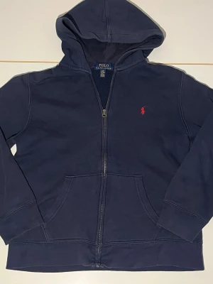 Mörkblå hoodie från Polo Ralph Lauren - Snygg mörkblå hoodie från Polo Ralph Lauren med dragkedja. Perfekt för dig som vill ha en stilren och bekväm look. Skick 6/10 