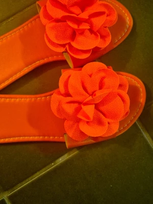 Orange Slippers with Flower, size 36 - A pair of orange slippers with a decorative flower on top. The slippers have a flat sole and are suitable for everyday use. Shipping same day if you order during opening hours of post office otherwise next day