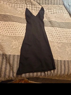 Svart slipklänning med tunna axelband - Svart slipklänning från h&m med tunna, korsade axelband och v-ringning. Klänningen har en slät och lätt struktur, är figurnära och har en enkel, stilren design. Perfekt för dig som gillar minimalistisk stil och vill ha något snyggt och bekvämt.