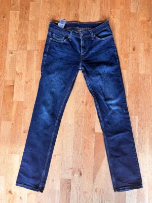 Levi's mörkblå slim fit jeans - Säljer ett par mörkblå slim fit jeans från Levi's med klassiska fem fickor och snygga kontrastsömmar. Jeansen har rak passform och är tillverkade i slitstarkt denim-material. Perfekta för dig som gillar en tidlös och clean look.