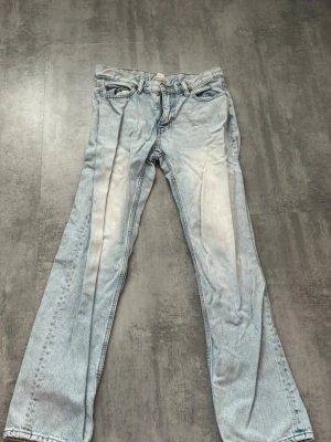 Ljusblå raka jeans - Säljer ett par ljusblå jeans med rak passform och klassisk femficksdesign. Jeansen har en blekt look med ljusa partier på framsidan och är tillverkade i denim. Perfekta för dig som gillar en avslappnad och trendig stil.