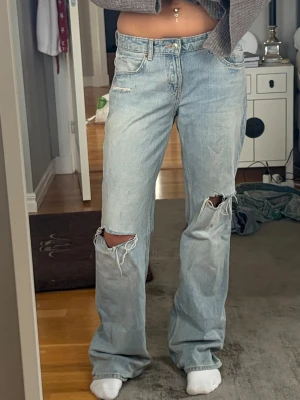 Baggy zara jeans - Säljer ett par ljusblå jeans med raka/vida ben och  hål vid knäna. Jeansen har klassisk femficksmodell, medel hög midja och slitna detaljer för en trendig look. Perfekta för dig som gillar en avslappnad och cool stil. Är från Zara och endast använda några gånger i storlek 38