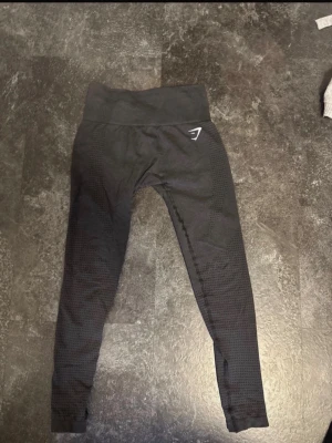 Svarta seamless leggings från Gymshark - Snygga svarta seamless leggings från Gymshark med hög midja och diskret mönstrad struktur längs benen. Stretchigt material som sitter tight och bekvämt, perfekt för träning eller chill. Gymshark-logga i vitt på höften.