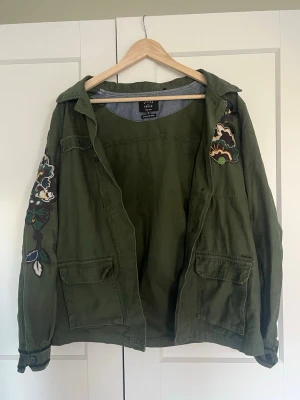 Grön broderad jacka - Cool grön jacka från Silver Creek med broderade blommor på axel och ärm. Jackan har två stora fickor framtill och klassisk krage. Perfekt för att ge din outfit en unik touch. Kan diskuter pris!😊