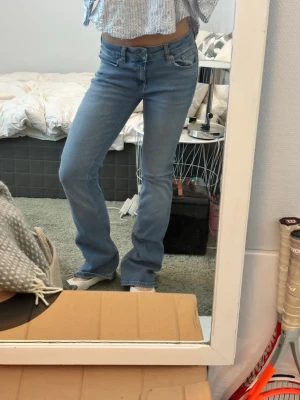 Ljusblå bootcut jeans - Säljer ett par ljusblå bootcut jeans med klassisk femficksdesign och normal midja. Jeansen har en snygg tvätt och är tillverkade i mjukt denimtyg med lite stretch för extra komfort. Perfekta för en avslappnad och trendig look.