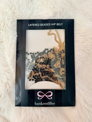 Hunkemöller Layered Beaded Hip Belt - Snygg midjekedja/höftbälte från Hunkemöller i flera lager med guldfärgade kedjor och svarta pärlor. Justerbar storlek med knäppe för perfekt passform. Oanvänd i originalförpackning. Nypris: 299kr