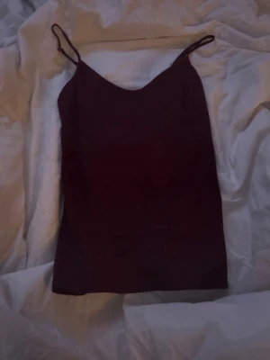 Vinröd  linnetopp med smala band - Snygg vinröd linnetopp med tunna axelband och v-ringad hals. Perfekt att styla till jeans eller kjol för en enkel men trendig look. Toppens material känns mjukt och följsamt mot huden.