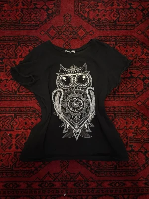 Svart t-shirt med ugglemotiv - Cool svart t-shirt med ett stort vitt ugglemotiv på framsidan. T-shirten har rund hals och korta ärmar, och är tillverkad i mjuk bomull. Perfekt för dig som gillar unika prints och vill sticka ut lite extra.
