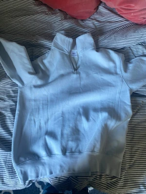 Ljusblå hoodie med halv dragkedja - Ljusblå hoodie från Zara med halv dragkedja framtill och hög krage. Tröjan har en enkel och clean design utan tryck eller mönster, tillverkad i mjukt bomullsmaterial. Perfekt för en avslappnad och cool look.