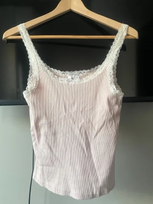 Ljusrosa ribbad linnetopp med spets - Säljer en ljusrosa ribbad linnetopp från H&M med tunna axelband och fina spetsdetaljer runt halsringningen och axelbanden. Materialet är mjukt och stretchigt. Super snygg och i ett väldigt bra skick❣️