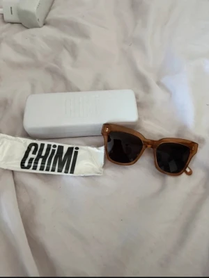 solglasögon från CHIMI - Snygga solglasögon från CHIMI med brun, transparent plastbåge och mörka linser. Modellen har en klassisk fyrkantig form och kommer med originalfodral och putsduk. Perfekt för att höja din stil under soliga dagar. Model 005 I peach 