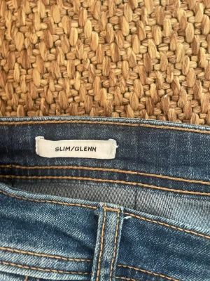 Slim Glenn blå jeans - Blå slim fit jeans med klassisk femficksdesign och snygga slitningar. Jeansen har kontrastsömmar och är tillverkade i denim med stretch för extra komfort. Perfekt passform och modern look för dig som gillar stilrena jeans.