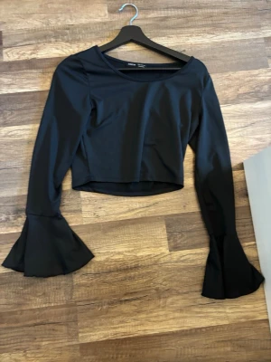 Svart topp med trumpetärmar från SHEIN - Cool svart topp från SHEIN med croppad passform och långa trumpetärmar som ger en unik look. Perfekt för dig som vill sticka ut och ha något trendigt i garderoben. Materialet är mjukt och känns skönt mot huden.
