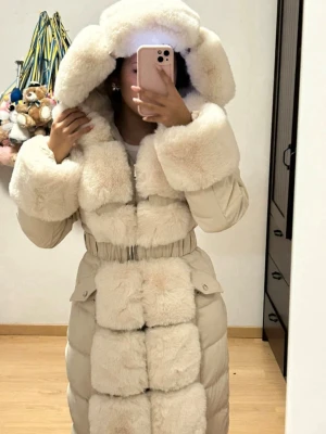 Lång beige pälsjacka med huva - Säljer en lång och riktigt fluffig beige pälsjacka med stor huva och breda pälsdetaljer på ärmar, bröst och längs hela framsidan. Jackan har en markerad midja med elastiskt band och praktiska fickor med lock. Perfekt för kalla vinterdagar. Är i storlek M men passar mig som har storleken XS