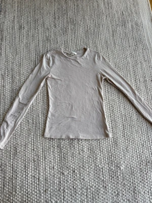 Ljusbeige långärmad topp från H&M - Ljusbeige långärmad topp från H&M i storlek XS. Toppen har en enkel och slim passform med rund halsringning och är gjord i mjuk bomull. 