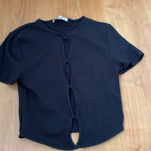 Svart kortärmad topp med knytning - Snygg svart topp från New yorker med korta ärmar och unik knytning framtill. Perfekt för en trendig look.