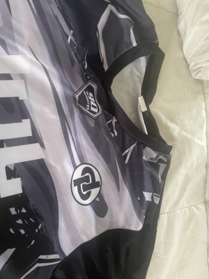 Svart JUL tröja - Snygg svart från DL Sports med grafiskt mönster i vitt, grått, gult och rött. Tröjan har korta ärmar, rund hals och är tillverkad i ett lätt och ventilerande material 