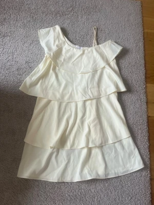 Ljusgul volangklänning Gina Tricot - Söt ljusgul kortklänning från Gina Tricot med flera volanger och asymmetrisk axel, där ena sidan har smalt axelband. Perfekt för sommarens varma dagar och har en luftig känsla tack vare det tunna materialet. Använd en gång