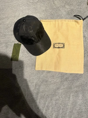 Svart keps från Gucci med monogram - Snygg svart keps från Gucci med klassiskt GG-monogram i materialmix av mesh och tyg. Kepsen har böjd skärm och justerbar baksida. Medföljer original dustbag och tagg. Perfekt för dig som vill ha en exklusiv och trendig accessoar.
