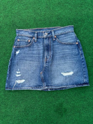 Blå jeanskjol från Levi's - Säljer en klassisk blå jeanskjol från Levi's med slitna detaljer som är perfekt inför sommarn🙏 Mått finns på bilden!! Kolla innan köp. PRIS KAN DISKUTERAS 