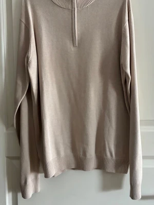 Beige halvzip tröja i bomull - Stilren beige tröja med halvzip och ribbade muddar vid ärmslut, hals och nederkant. Tillverkad i mjuk bomull och har en relaxed passform. Perfekt för lager på lager och enkel att matcha med olika outfits.