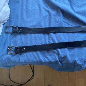 Säljer två läder skärp för men skicka om du bara vill ha ett så kan vi diskutera ett pris - Säljer ett stilrent svart bälte i skinn med silverfärgat spänne. Bältet har en enkel och clean design utan mönster, perfekt till jeans eller kostymbyxor. Spännet är fyrkantigt och bältet har flera hål för justerbar passform.