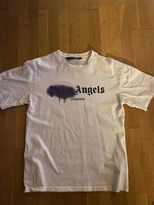 Vit Palm Angels t-shirt London print - Säljer en vit t-shirt från Palm Angels med svart och blått 'London' tryck på bröstet. Nytt skick inte använd mer än 5 gånger. Den är storlek M men kan passa olika.
