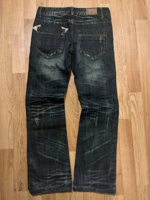 Archive jeans nudie style - Säljer ett par mörkblå jeans från Edwin med raka ben och slitna detaljer. Jeansen har klassiska fem fickor, kontrastsömmar och en cool tvätt med tydliga whiskers och slitningar. Perfekta för en avslappnad streetstil.