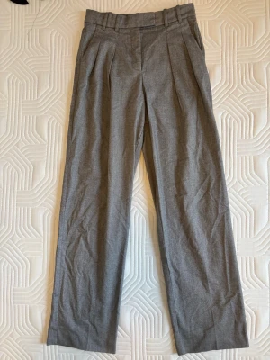 Grå kostymbyxor från Mango - Snygga grå kostymbyxor från Mango med hög midja, pressveck och vida ben. Byxorna har hällor för skärp och sidofickor. 