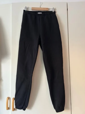 Svarta mjukisbyxor med resår - Säljer ett par svarta mjukisbyxor med resår i midjan och vid bensluten. Byxorna har en klassisk rak passform och är tillverkade i ett mjukt material som är perfekt för chill dagar. Inga synliga loggor eller detaljer, enkel och stilren design.