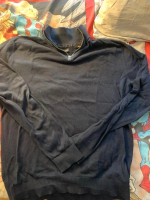 Mörkblå quarter zip tröja Jack & Jones - Mörkblå tröja från Jack & Jones med quarterzip dragkedja vid halsen. Tröjan har långa ärmar, ribbade muddar och är tillverkad i ett mjukt material. Perfekt för lager på lager och enkel att matcha med olika outfits.