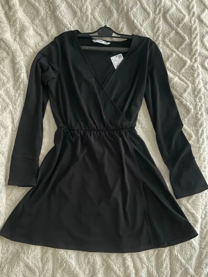 Svart omlottklänning med lång ärm, S - Stilren svart omlottklänning med långa ärmar och v-ringad hals. Storlek S, Mango. Klänningen har resår i midjan för en smickrande passform och är tillverkad i ett mjukt, lätt material. Perfekt för dig som gillar enkel men snygg design.