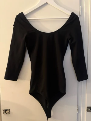 Svart body från Gina Tricot - Säljer en svart body från Gina Tricot med 3/4-ärmar och bred, djup urringning både fram och bak. Tillverkad i stretchigt material som sitter tight och bekvämt. Perfekt att styla till jeans eller kjol för en enkel men snygg look.