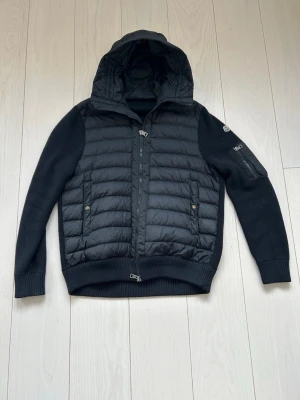 Svart hybrid cardiganjacka Moncler - Snygg svart cardiganjacka från Moncler med stickade ärmar och quiltad front. Str XL som passar 185-200cm. Tyvärr har taggen i nacken ramlat av därav det låga priset 