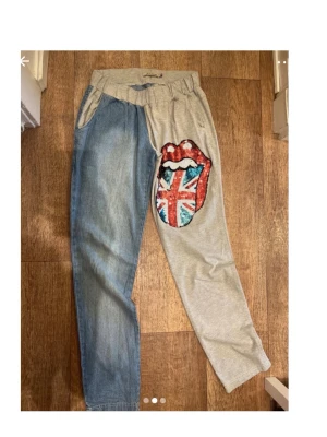 Blue jeans - Snygga byxor med ena benet i ljusblå denim och andra i grått tyg. På det grå benet finns en stor applikation med läppar och Union Jack-flagga i paljetter. Resår i midjan och avslappnad passform. Perfekt för dig som gillar statement-plagg.
