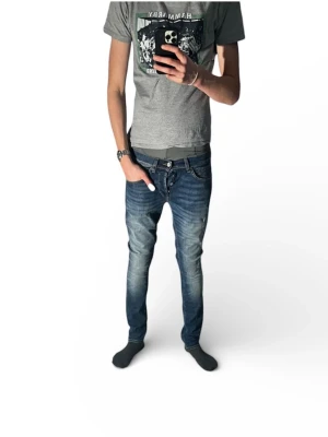 Blå slim fit jeans från Dondup George - Säljer ett par klassiska blå jeans från Dondup med raka ben och snygga slitningar på låret. Jeansen har fem fickor, normal passform och är tillverkade i mjukt bomullsmaterial. Perfekta för en avslappnad och stilren look. Modell george. Helt nya med schyssta slitningar.