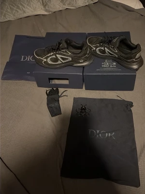 Svarta Dior B30 sneakers - Säljer ett par svarta Dior B30 sneakers med reflekterande silverdetaljer och tydlig CD-logga på sidan. Skorna har en sportig siluett, mesh och syntetmaterial samt bekväm vadderad insida. Kommer med originalkartong, dustbag och extra skosnören.
