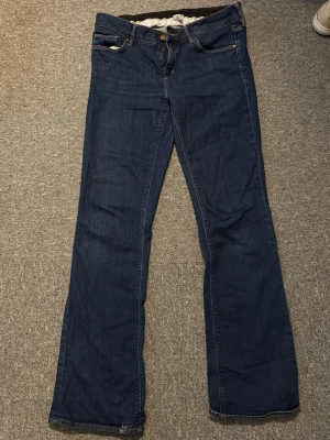 Mörkblå bootcut jeans från H&M - Säljer ett par mörkblå bootcut jeans från H&M i klassisk denim. Jeansen har fem fickor, normal midja och vida ben. Snygga kontrastsömmar och knappgylf. Perfekta för en avslappnad och trendig look.
