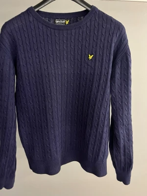 Mörkblå tröja Lyle & Scott - Mörkblå tröja från Lyle & Scott med rund halsringning och gul logga broderad på bröstet. Tröjan har ribbade muddar vid ärmslut och nederkant, och passar perfekt till höst och vinter. Storlek: S. Hör av dig om du undrar något mer. 🤩