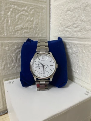 Silverfärgad klocka från Guess - Stilren klocka från Guess med silverfärgat metallarmband och vit urtavla. Klockan har flera små urtavlor för datum och 24-timmarsvisning. Klassisk rund form och tydliga markeringar. Perfekt accessoar för dig som gillar en clean look.